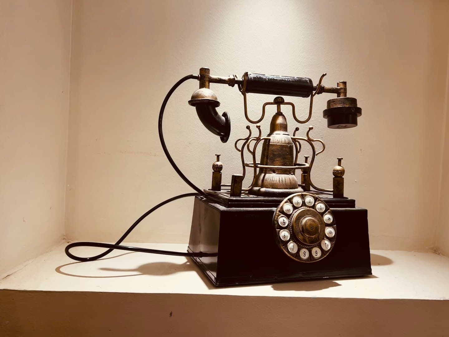 Teléfono antiguo de latón y negro con timbre sobre un estante.