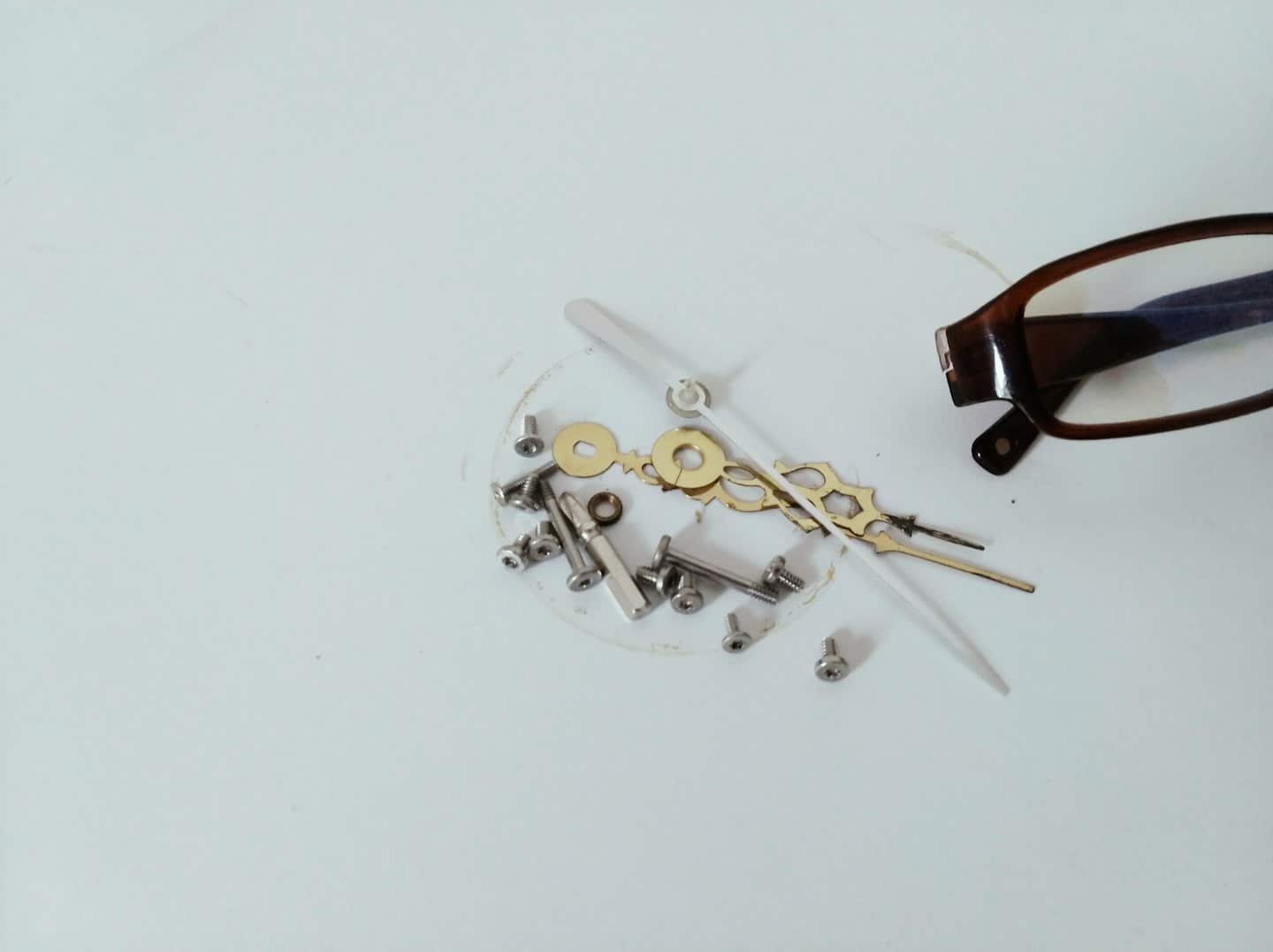 Partes de reloj y gafas sobre una superficie blanca.