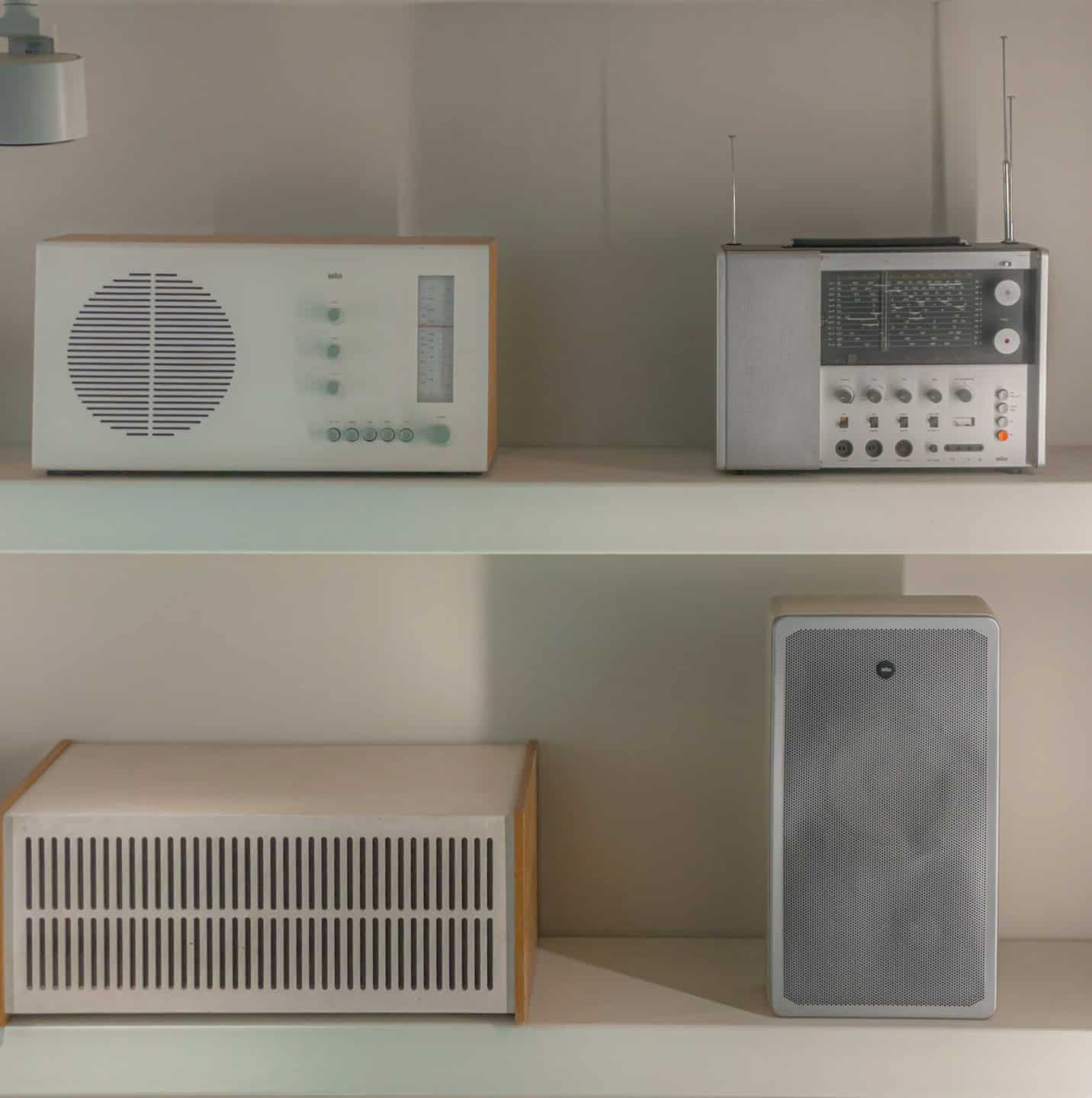 Radios antiguos y un amplificador descansan sobre estantes blancos.
